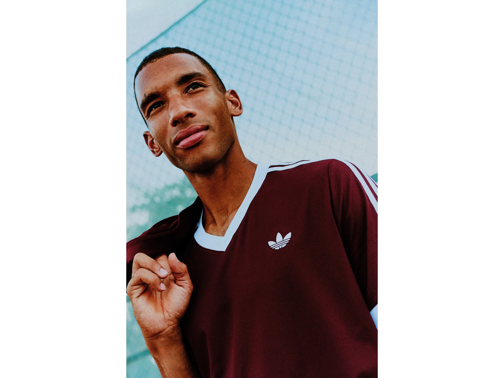 A model wearing a maroon adidas Classics tennis shirt beside a court